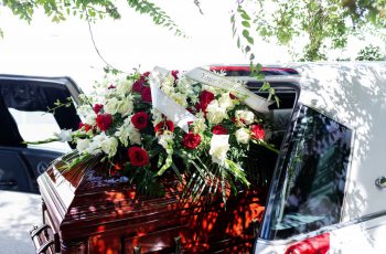 Imagem de um caixão no carro com uma coroa de flores e uma faixa em cima