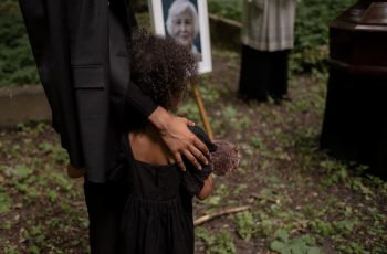 Imagem de uma criança em um velório olhando o quadro de uma senhora