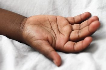 Imagem de uma mão de uma pessoa na cama com lençol branco