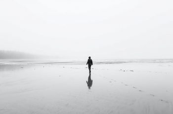 Imagem de um homem andando na praia deserta em um dia de chuva