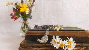 imagem de um caixão com flores nas laterais, uma coroa de flores pequena, um relógio de bolso e o fundo branco. Capa do conteúdo sobre serviços funerários