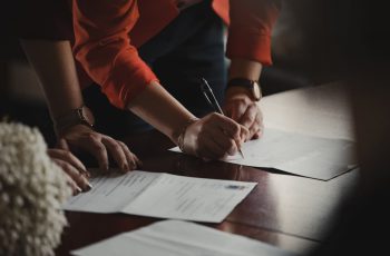 Duas pessoas assinando documentos em uma mesa de madeira