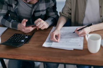 Imagem de duas pessoas calculando as contas em uma mesa de madeira