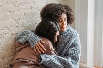 Imagem de duas mulheres abraçadas com aparência triste