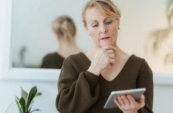 Uma mulher com o fundo branco olhando pensativa para o tablet