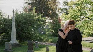 Mulher em um velório consolando mãe que perdeu o filho.